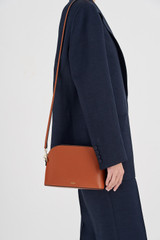 Profile view of model wearing the Oroton Inez Slim Crossbody in Cognac and Shiny Soft Saffiano for Women .
