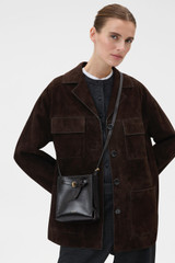 Profile view of model wearing the Oroton Margot Tiny Bucket Bag in Dark Chocolate and Premium pebble leather for Women .