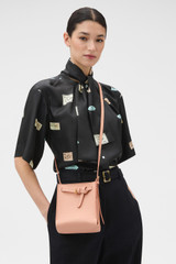 Profile view of model wearing the Oroton Margot Tiny Bucket Bag in Melon and Premium crackle leather for Women .
