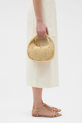 Profile view of model wearing the Oroton Clara Straw Mini Bag in Natural and Woven straw material for Women .