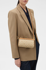 Profile view of model wearing the Oroton Harvey Signature Baguette Crossbody in Stone/Tan and Nylon canvas base cloth material with PVC coating (70% PVC, 30% polyester) for Women .
