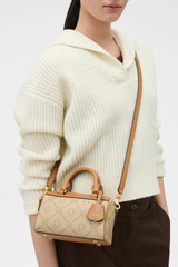 Profile view of model wearing the Oroton Harvey Signature Tiny Barrel Bag in Stone/Tan and Nylon canvas base cloth material with PVC coating (70% PVC, 30% polyester) for Women .