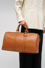 Profile view of model wearing the Oroton Wanderer Weekender in Amber and Premium smooth leather for Women .