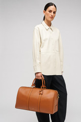 Profile view of model wearing the Oroton Wanderer Weekender in Amber and Premium smooth leather for Women .