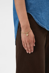 Profile view of model wearing the Oroton Heart Charm Bracelet in Gold and Premium brass material for Women .