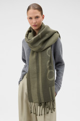 Profile view of model wearing the Oroton Heather Light Weight Wool Scarf in Olive and 50% acrylic and 50% wool blend fabric for Women .
