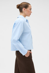 Profile view of model wearing the Oroton Oxford Cropped Shirt in Soft Blue and 100% cotton fabric for Women .