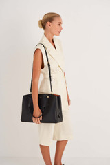 Profile view of model wearing the Oroton Anika 13" Day Bag in Black and Pebble leather for Women .