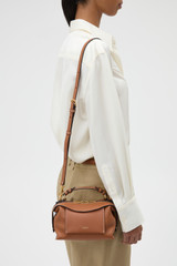 Profile view of model wearing the Oroton Mica Mini Bowler in Brandy and Premium pebble leather for Women .
