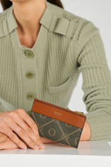 Profile view of model wearing the Oroton Harvey Signature Mini 4 Credit Card Zip Pouch in Black/Cognac and Nylon canvas base cloth material with PVC coating (70% PVC, 30% polyester) for Women .