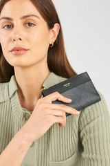 Profile view of model wearing the Oroton Harvey Signature 12 Credit Card Zip Wallet in Black and Nylon canvas base cloth material with PVC coating (70% PVC, 30% polyester) for Women .