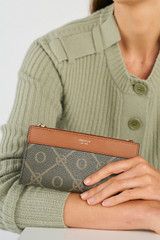 Profile view of model wearing the Oroton Harvey Signature Slim Zip Wallet in Black/Cognac and Nylon canvas base cloth material with PVC coating (70% PVC, 30% polyester) for Women .