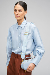 Profile view of model wearing the Oroton Logo Bag Strap in Washed Denim and Premium leather and webbing material for Women .