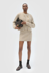 Profile view of model wearing the Oroton Nep Knit Mini Skirt in Oat and 65% merino wool, 30% nylon, and 5% alpaca blend fabric for Women .