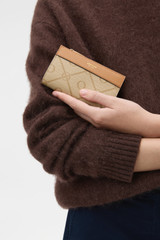 Profile view of model wearing the Oroton Harvey Signature 12 Credit Card Zip Wallet in Stone/Tan and Nylon canvas base cloth material with PVC coating (70% PVC, 30% polyester) for Women .