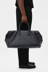 Profile view of model wearing the Oroton Voyager Coated Nylon Weekender in Black and 100% polyester fabric for Men .