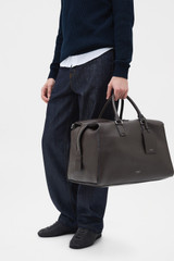 Profile view of model wearing the Oroton Paxton Weekender in Dark Chocolate and Premium pebble leather for Men .