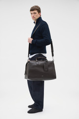 Profile view of model wearing the Oroton Paxton Weekender in Dark Chocolate and Premium pebble leather for Men .