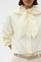 Profile view of model wearing the Oroton Scallop Tie Neck Shirt in Whipped Cream and 100% soft cotton fabric for Women .