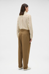 Profile view of model wearing the Oroton Tapered Pleat Pant in Dark Rye and 97% wool and 3% spandex blend fabric for Women .