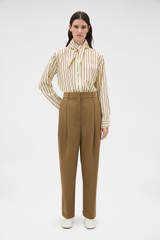 Profile view of model wearing the Oroton Tapered Pleat Pant in Dark Rye and 97% wool and 3% spandex blend fabric for Women .