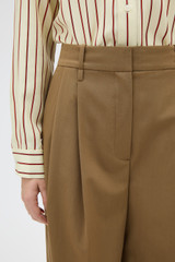 Profile view of model wearing the Oroton Tapered Pleat Pant in Dark Rye and 97% wool and 3% spandex blend fabric for Women .