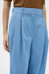 Profile view of model wearing the Oroton Tapered Pleat Pant in Porcelain Blue and 97% wool and 3% spandex blend fabric for Women .