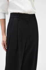 Profile view of model wearing the Oroton Tapered Pleat Pant in Black and 100% wool fabric for Women .