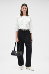 Profile view of model wearing the Oroton Tapered Pleat Pant in Black and 100% wool fabric for Women .