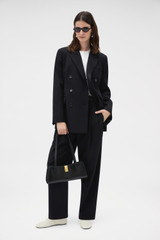 Profile view of model wearing the Oroton Tapered Pleat Pant in Black and 100% wool fabric for Women .