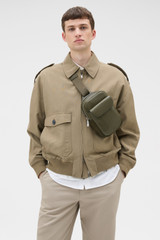 Profile view of model wearing the Oroton Oscar Pebble Crossbody in Forest Green and Premium pebble leather for Men .