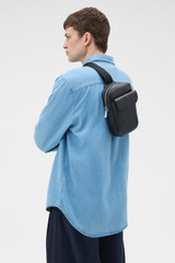 Profile view of model wearing the Oroton Oscar Pebble Crossbody in Black and Premium pebble leather for Men .