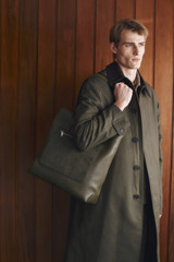 Profile view of model wearing the Oroton Oscar Pebble Tote in Forest Green and Premium pebble leather for Men .