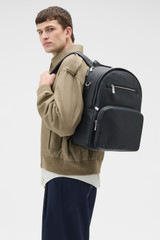 Profile view of model wearing the Oroton Oscar Pebble Backpack in Black and Premium pebble leather for Men .