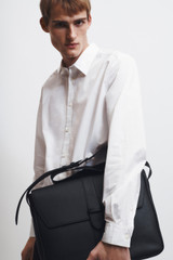 Profile view of model wearing the Oroton Nicholas Smooth Satchel Messenger in Black and Soft nappa cow leather for Men .