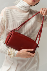 Profile view of model wearing the Oroton Charlie Smooth Shoulder Bag in Garnet and Smooth sheep leather for Women .