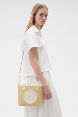 Profile view of model wearing the Oroton Polly Straw Small Tote in Natural/Cream and Woven straw material for Women .