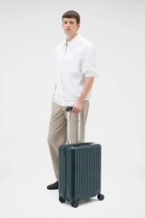 Profile view of model wearing the Oroton Jet Carry On Roller Case in Dark Evergreen and Durable polycarbonate shell for Women .