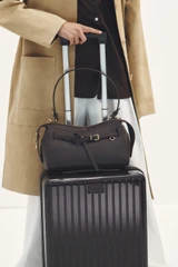 Profile view of model wearing the Oroton Jet Carry On Roller Case in Rich Umber and Durable polycarbonate shell for Women .