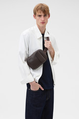 Profile view of model wearing the Oroton Oscar Pebble Crossbody in Dark Chocolate and Premium pebble leather for Men .