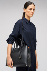 Profile view of model wearing the Oroton Muse Three Pocket Day Bag in Black and Premium saffiano and split calf leather for Women .