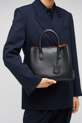 Profile view of model wearing the Oroton Muse Small Three Pocket Day Bag in Black and Saffiano And Smooth Leather for Women .