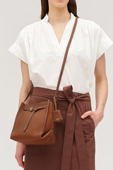 Profile view of model wearing the Oroton Margot Mini Bucket Bag in Whiskey and Pebble leather for Women .