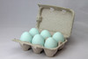 Six teal ceramic nest eggs in a brown paper pulp carton with grey background