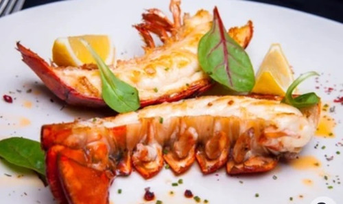 Cooked Florida Spiny Lobster tail served with fresh lemon wedges and leafy greens, showcasing tender white lobster meat prepared for serving.