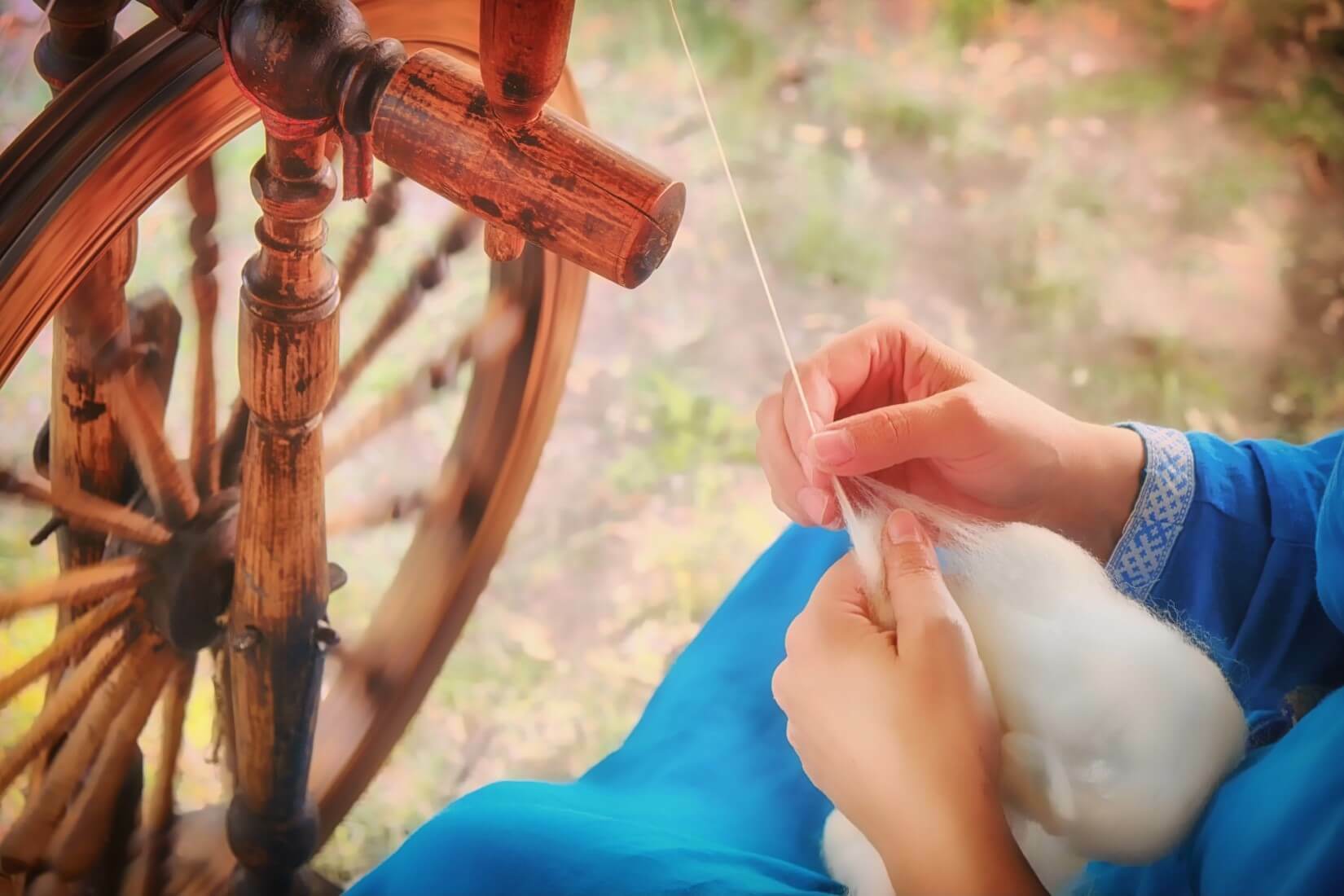 Person spinning wool on an old-fashioned spinning wheel outdoors.