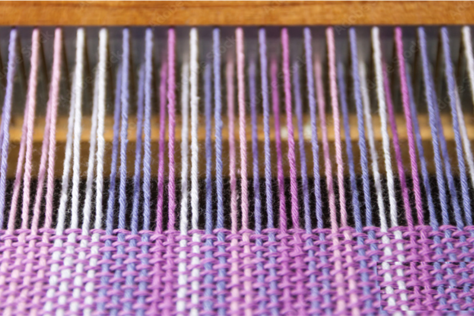 Close-up of a loom with colorful woven fabric and vertical yarn threads.