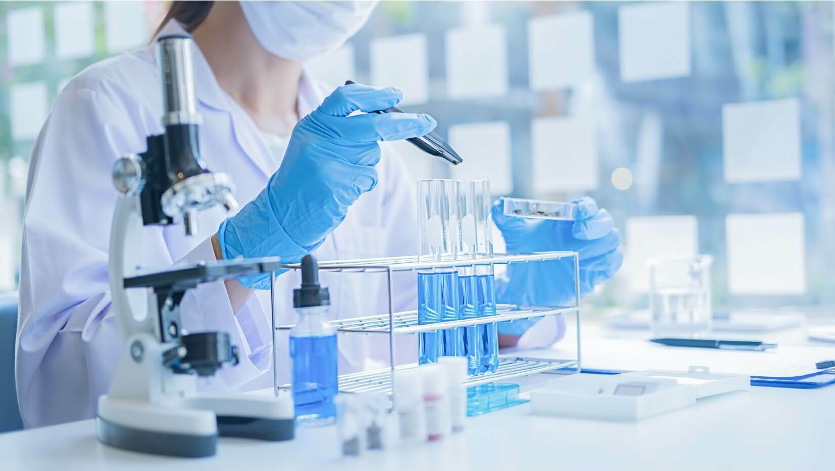 Scientist using a pipette with test tubes and microscope in a lab.