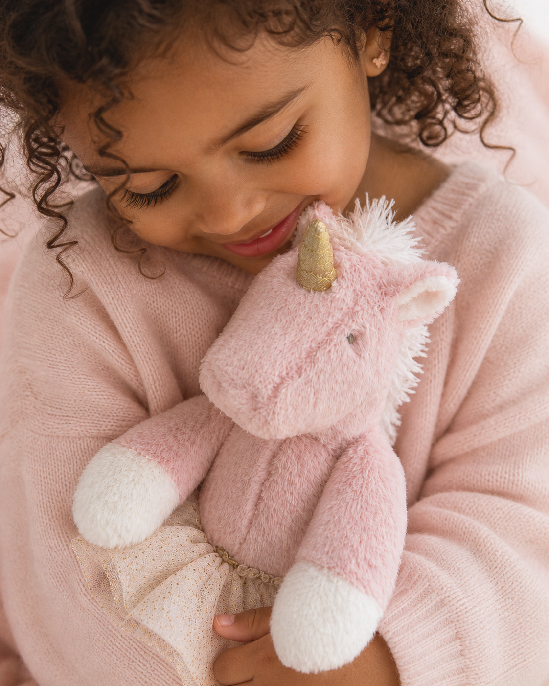 Little girl in a pink sweater hugging a plush pink unicorn toy
