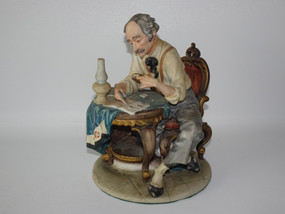 Vintage Italian Pucci porcelain The Stamp Collector figurine depicting a seated gentleman examining stamps beside a lamp and ornate table.